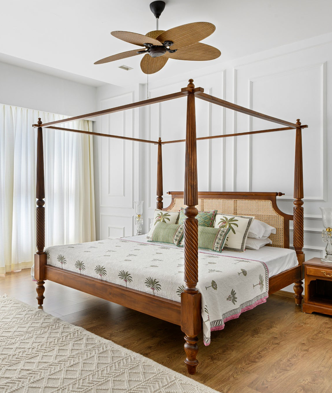 A four-poster bed made of wood and rattan, with a white bedsheet and green and white pillows, placed in a room with a ceiling fan.