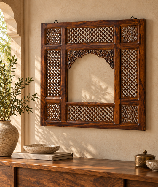 A dark brown carved wooden wall frame with intricate lattice and arch details, mounted on a beige wall above a wooden console table with decorative items.